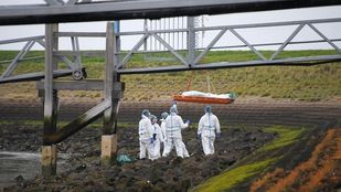 Mannen in witte pakken staan bij afgedekt lichaam dat omhoog wordt getakeld