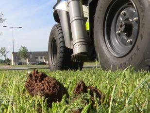 Close-up van een hondendrol met op de achtergrond de wielen en zuigmond van de poepquad