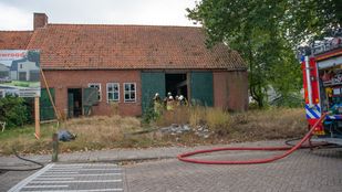 Op straat zie je nog net de achterkant van een brandweerauto met een uitgerolde rode brandslang en tussen de openstaande schuurdeuren van een oude boerderij met kapotte raampjes staan enkele brandweermensen