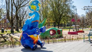 Kunstwerk van zittende blauwe olifant met geel-oranje clown op z'n buik en krullende slurf met daarop een wereldbol