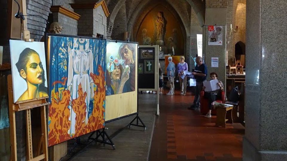 Grote schilderijen staan op schildersezels in het middenschip van een kerk