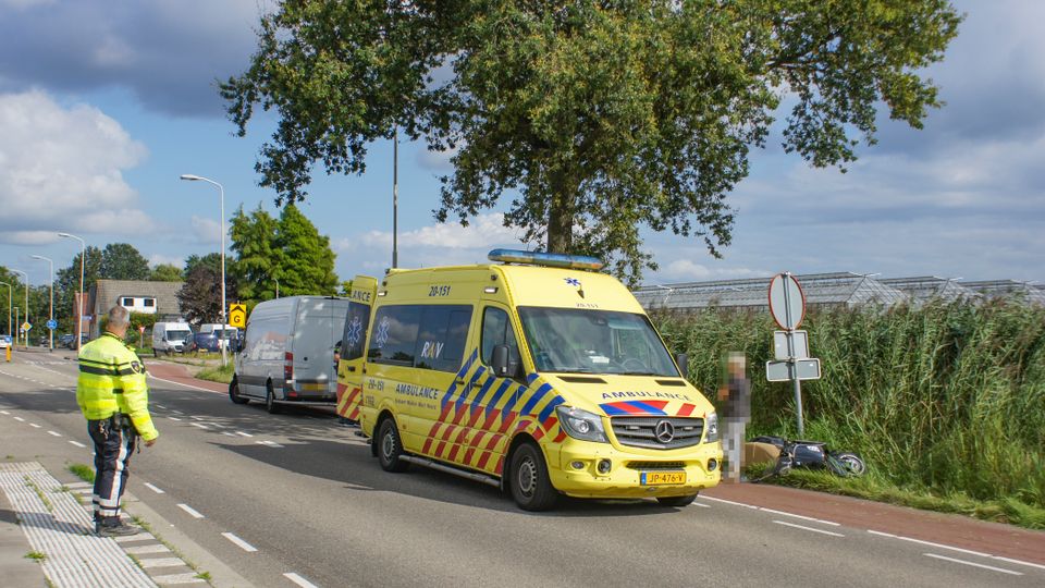Agent regelt het verkeer, aan de overkant van de weg staan een ambulance en een witte bestelbus en naast de ambulance ligt een scooter in het gras