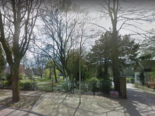 Ingang in hekwerk rond Emile van Loonpark in Roosendaal met op achtergrond bomen en vijver