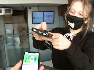 Vrijwilliger met mondkapje controleert toegangskaart op smartphone van bezoeker