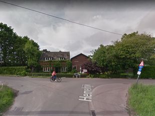 Fietser steekt vanaf links een t-splitsing over met op de achtergrond een woning