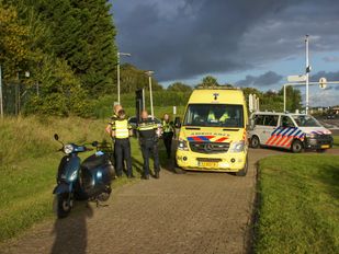Op een fietspad naast een greppel staat een scooter met daarachter een ambulance, politiewagen en enkele hulpverleners