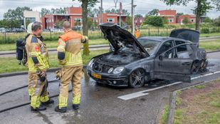 Twee brandweermensen in gele pakken staan bij zwarte uitgebrande auto waarvan de motorkap, deuren en kofferbak wijd open staan