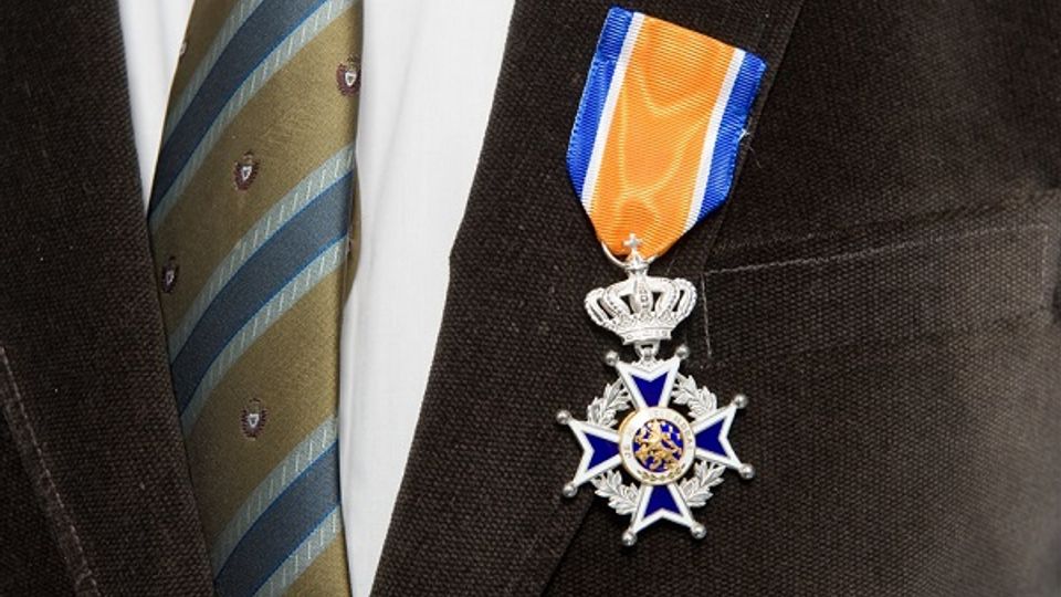 Close-up van koninklijke onderscheiding opgespeld op het rever van een zwart colbert