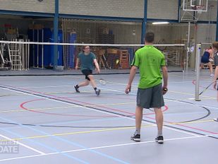 Sporthal met badmintonveld waar vier mensen een dubbelspel spelen